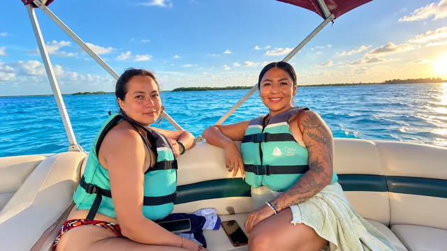 Dos viajeras con chalecos sentadas en un pontón con la laguna al fondo.