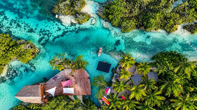 Vista aérea de Los Rápidos de Bacalar, con agua turquesa, vegetación y una terraza junto al canal.
